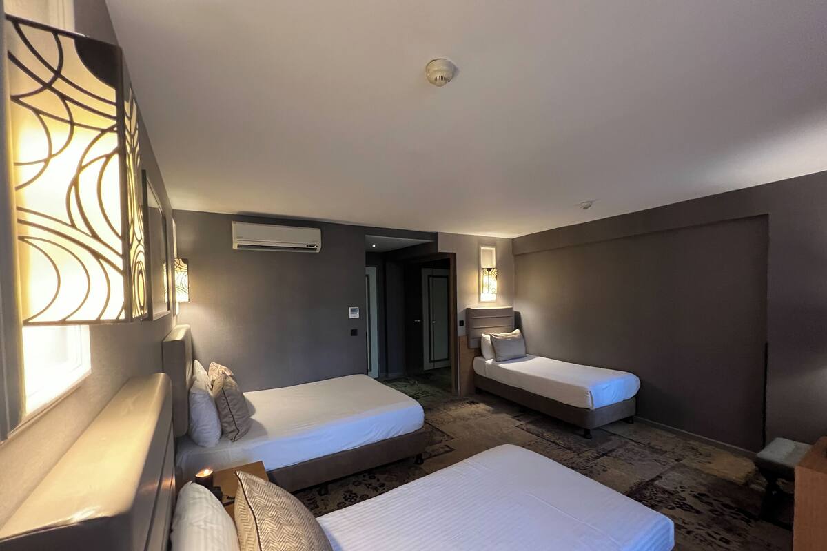 Habitación de hotel con dos camas individuales, un sofá, un escritorio y un ventanal grande.