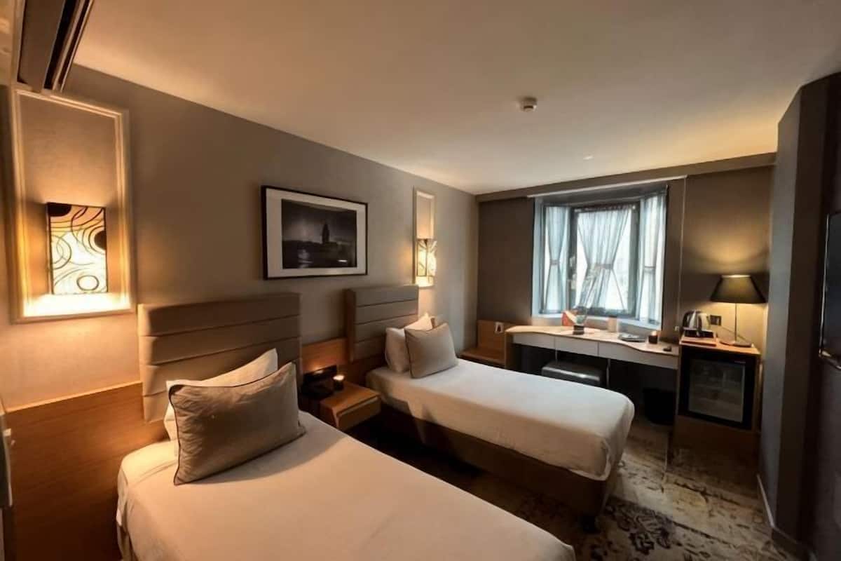 Habitación de hotel con dos camas, un escritorio, una silla, una lámpara y un cuadro en la pared.