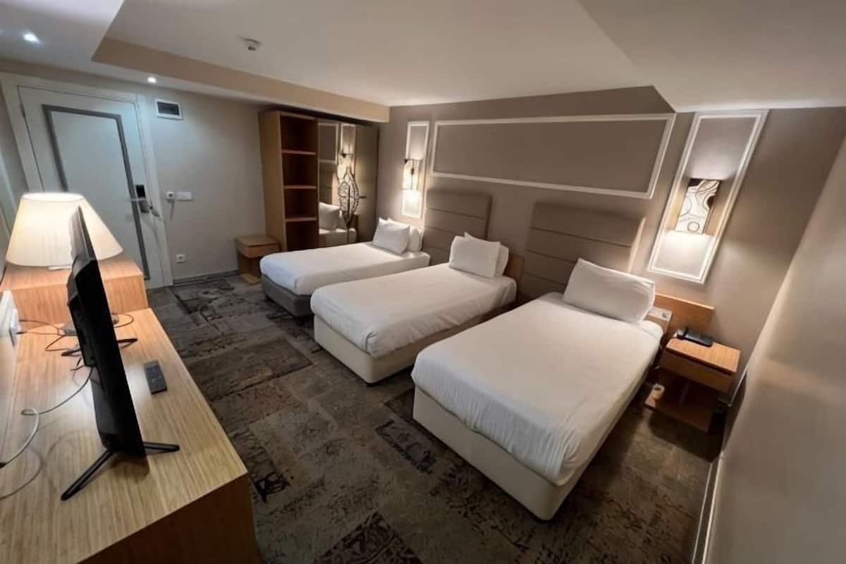 Habitación de hotel con dos camas, un escritorio con computadora, televisor y armario.