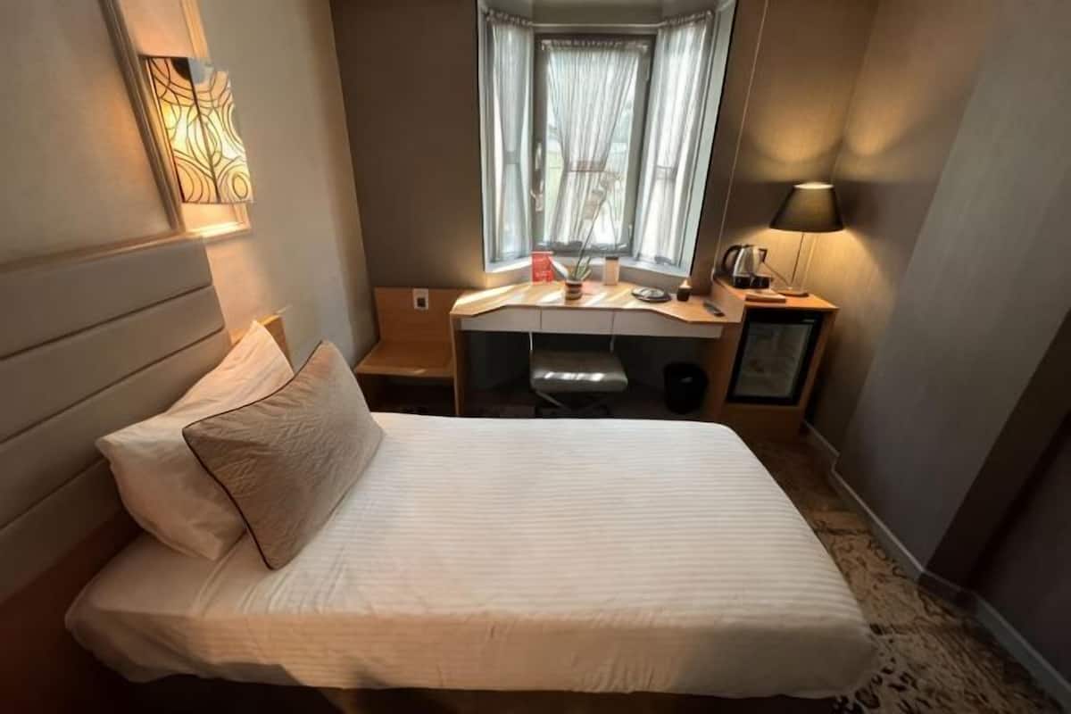 Habitación de hotel con cama, escritorio y ventana con cortinas.