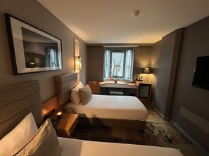 Ein Hotelzimmer mit einem großen Bett, einem Nachttisch, einer Lampe und einem Schreibtisch mit Stuhl.