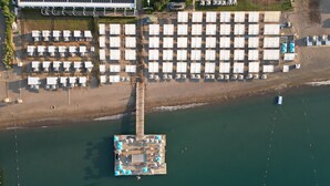 Vista aérea de un resort frente a la playa, con varias filas de sombrillas, un muelle y un edificio de techo plano.
