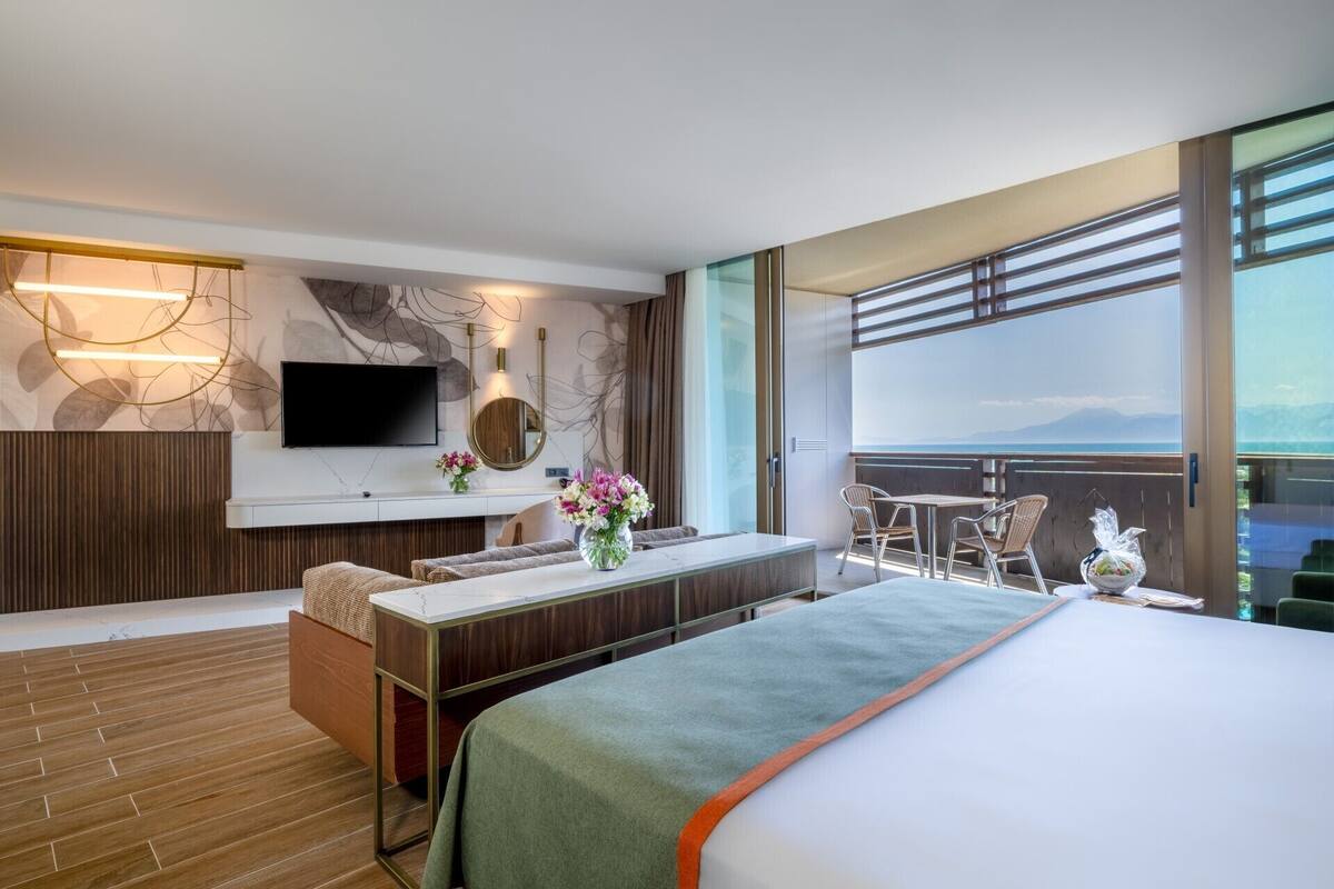 Una habitación de hotel moderna con una cama grande, un escritorio con una silla, un televisor y un balcón con vistas.