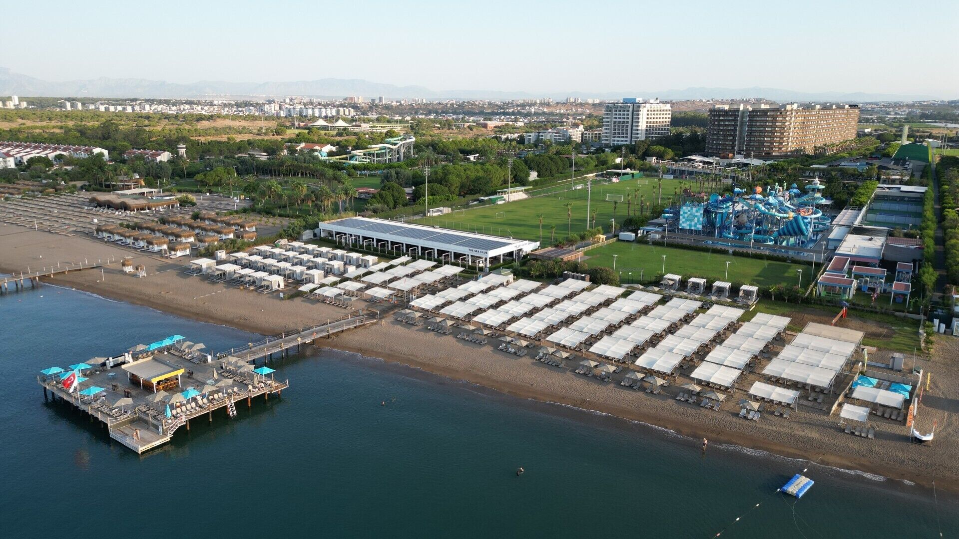 An aerial view of a coastal resort with a marina, beach umbrellas, and a water park.