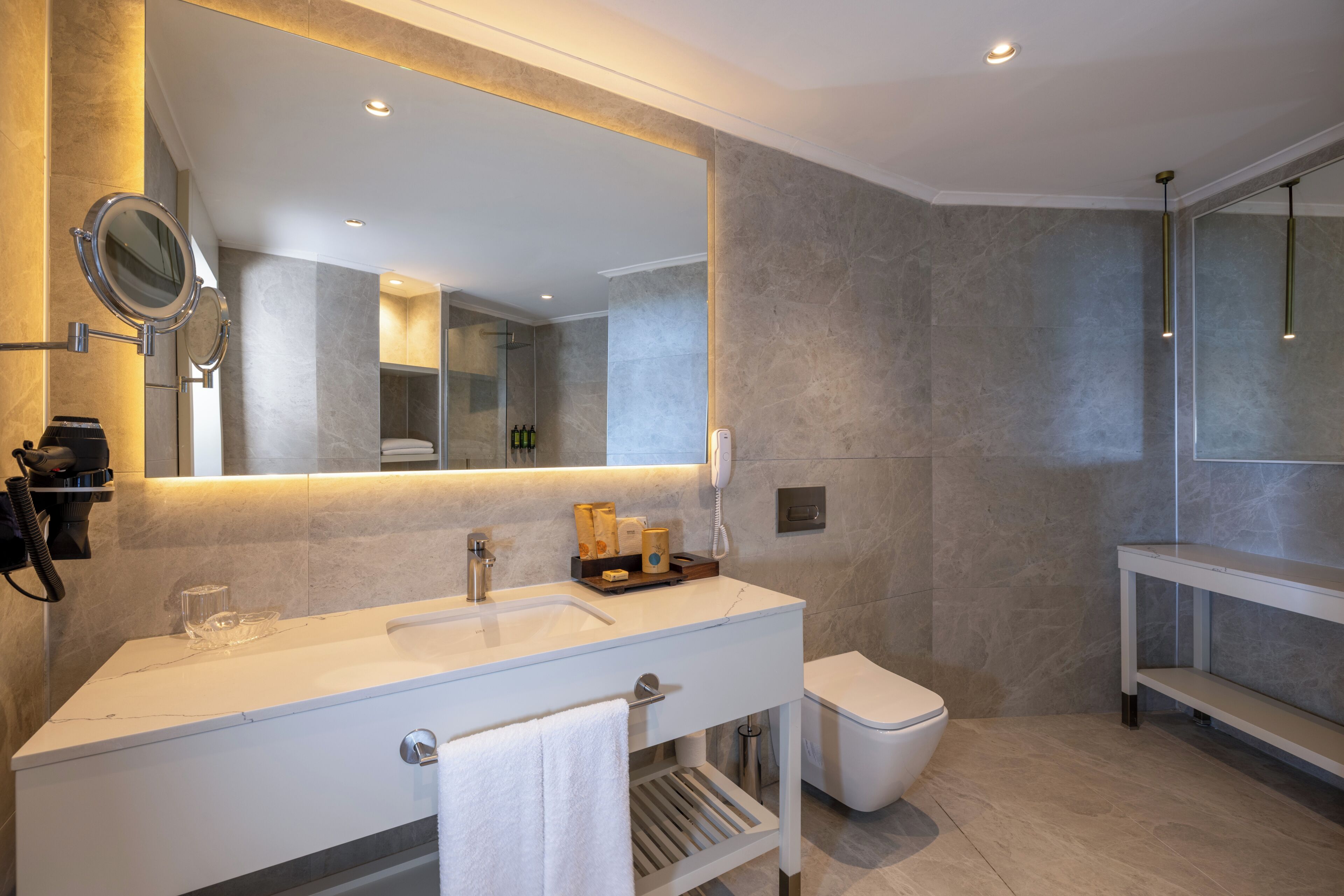 A modern bathroom with a large mirror, a sink, a toilet, and a shower area.
