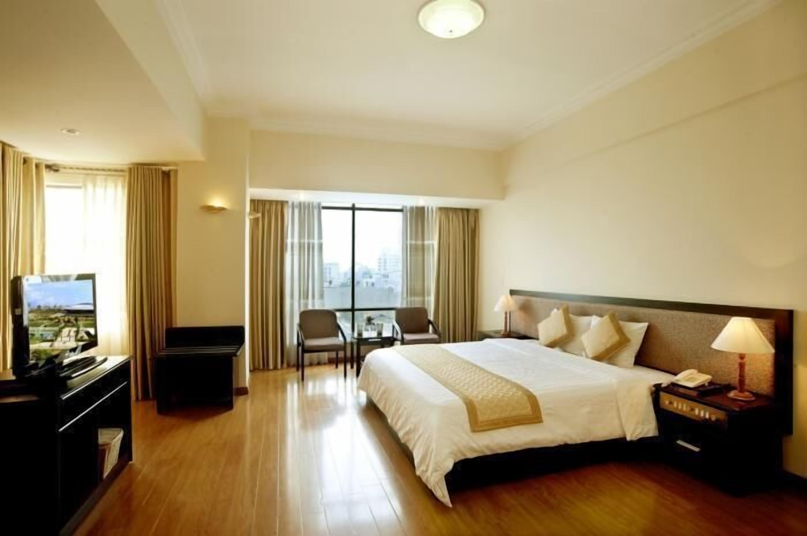A hotel room with a large bed, a desk with a television, a chair, and a window with curtains.