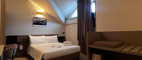 A compact hotel room with a bed, a desk, and a chair.