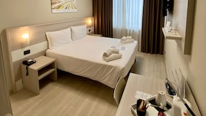 A hotel room with a large bed, bedside tables, a desk with a tray of amenities, a painting on the wall, and a window with curtains.