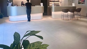 A modern hotel lobby with a reception desk, seating area, and a large illuminated ceiling feature.