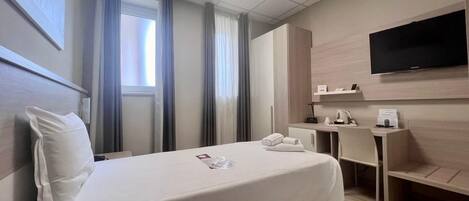Una habitación de hotel con cama, escritorio, televisor y ventana con cortinas.