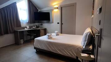 A hotel room with a bed, a desk, a chair, a television, and a wardrobe.