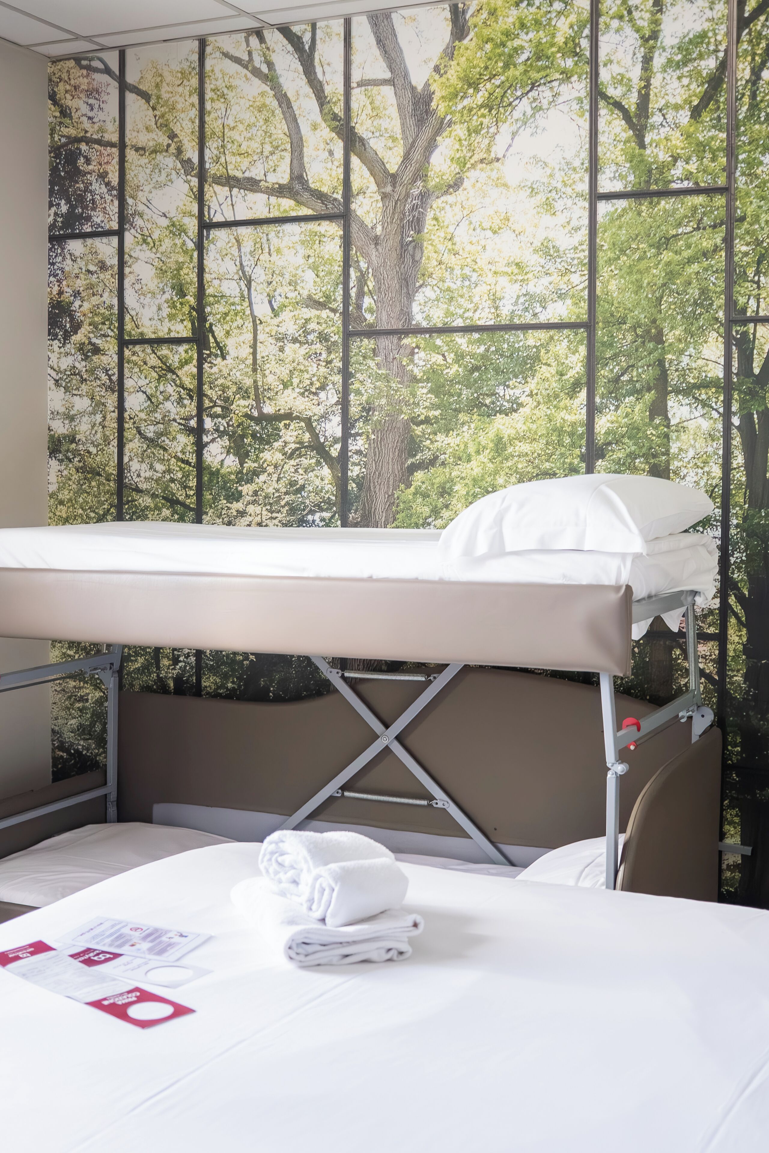 A hospital room with a bed, a table with a folded towel, and a window with a tree view.