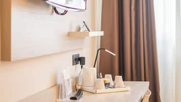 Habitació d'hotel amb escriptori de fusta, televisió penjada, petita estant amb articles de tocador i finestra amb cortines.