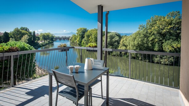 A balcony with a table and chairs, overlooking a river and greenery.