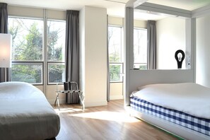 A hotel room with two beds, large windows, a chair, and a wall-mounted light fixture. - Qbic Hotel Amsterdam WTC (Amsterdam)