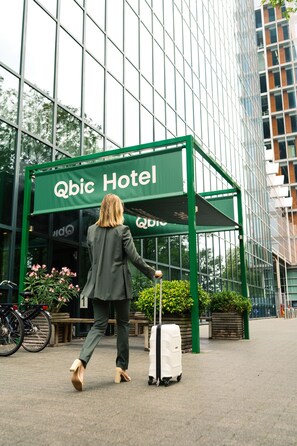 A woman in a suit walking towards a hotel entrance with a green awning labeled "Qbic Hotel". - Qbic Hotel Amsterdam WTC (Amsterdam)