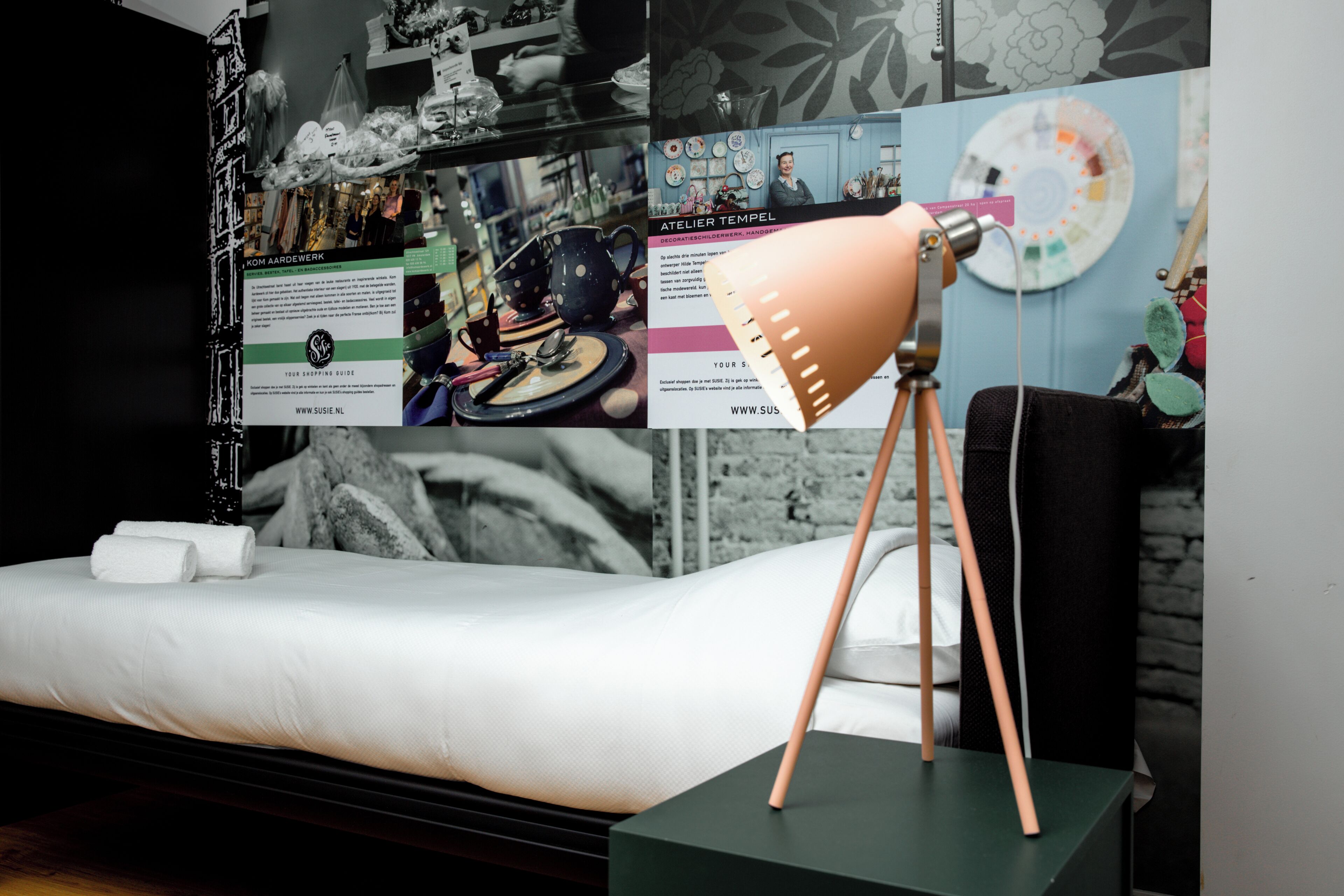 Una habitación moderna con una cama, una mesita de noche verde y una pared decorada con varios objetos y un póster.