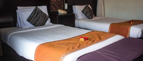 Two single beds with white linens and decorative pillows, a wooden headboard, and a small nightstand with a telephone.