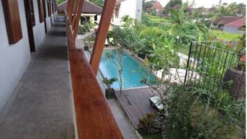 Uma área à beira da piscina com um deck de madeira, piscina e vegetação ao redor.
