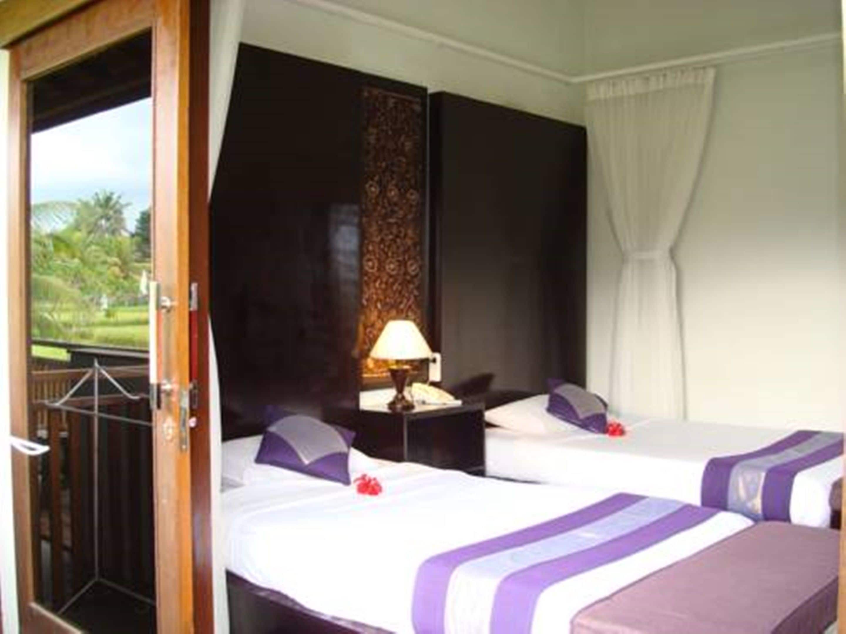 Une chambre d’hôtel avec deux lits, une table de chevet, une lampe et une vue sur la verdure.