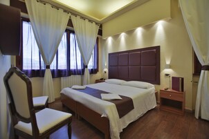 Habitación de hotel con una cama grande, una mesita de noche de madera, una silla y una ventana con cortinas.