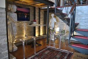 Un interior moderno con una escalera, sillas de vidrio transparente y una estatua.