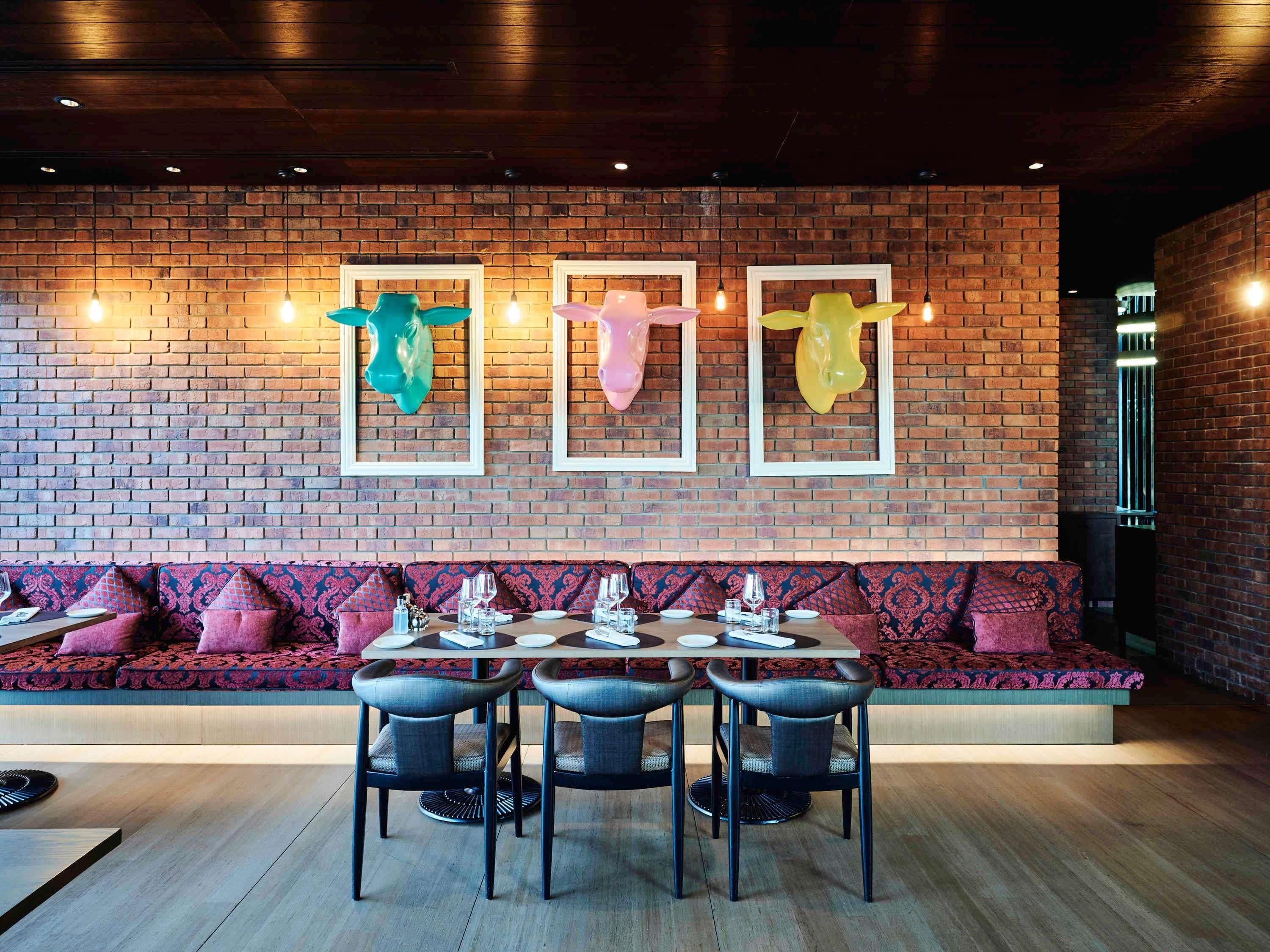 A restaurant with a brick wall, colorful animal head sculptures, a long bench seating area, and a round table with chairs.