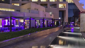 A modern hotel with a pool, outdoor seating, and a well-lit facade.