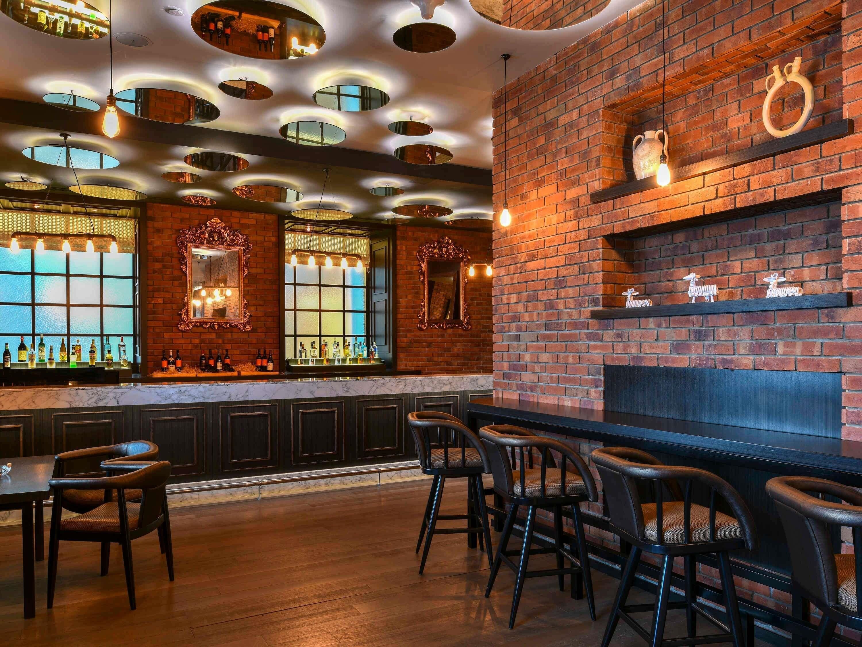 A bar area with a brick wall, shelves with bottles, and a seating area with chairs.