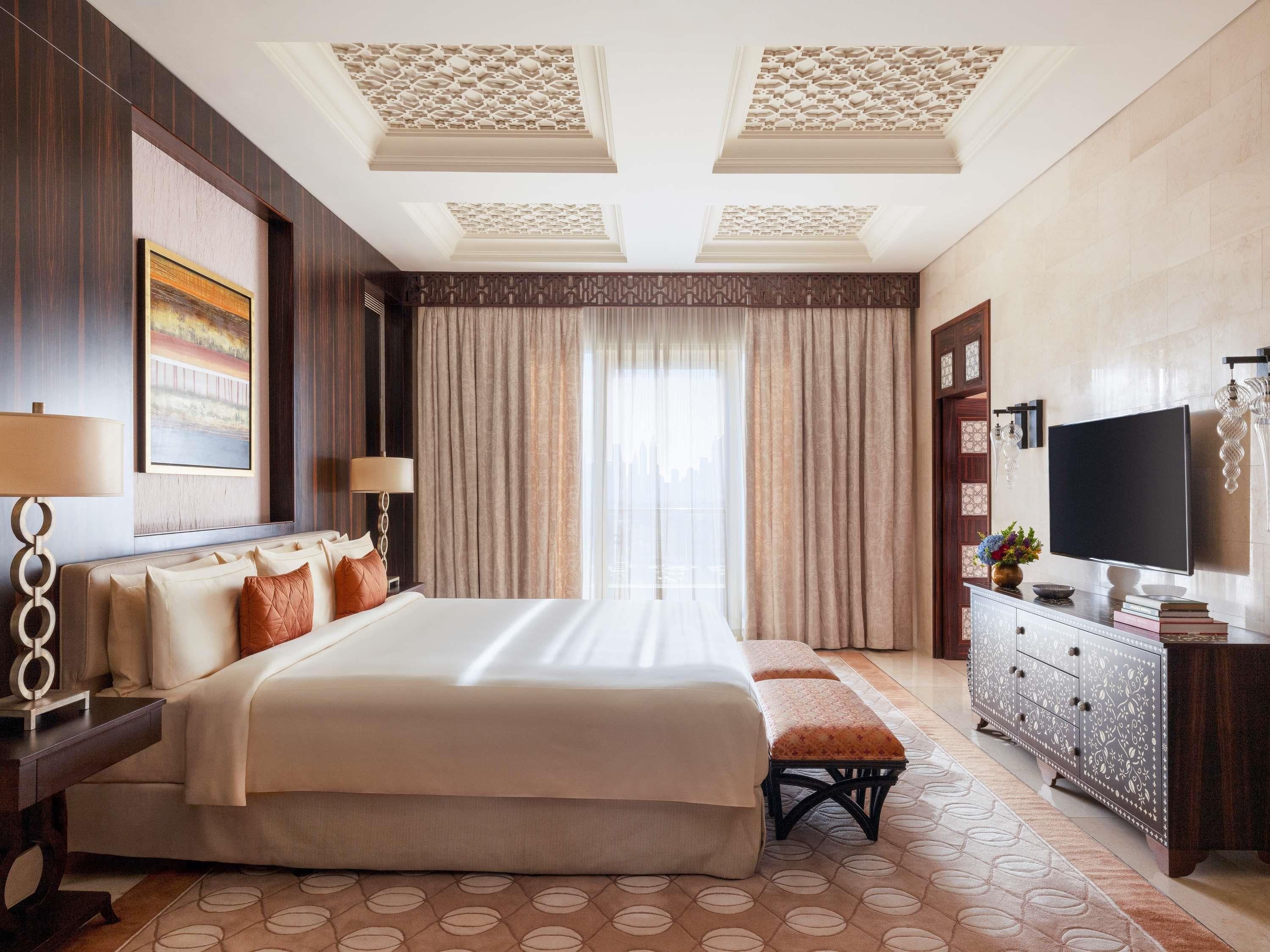 A hotel room with a large bed, a TV, a desk, and a window with curtains.