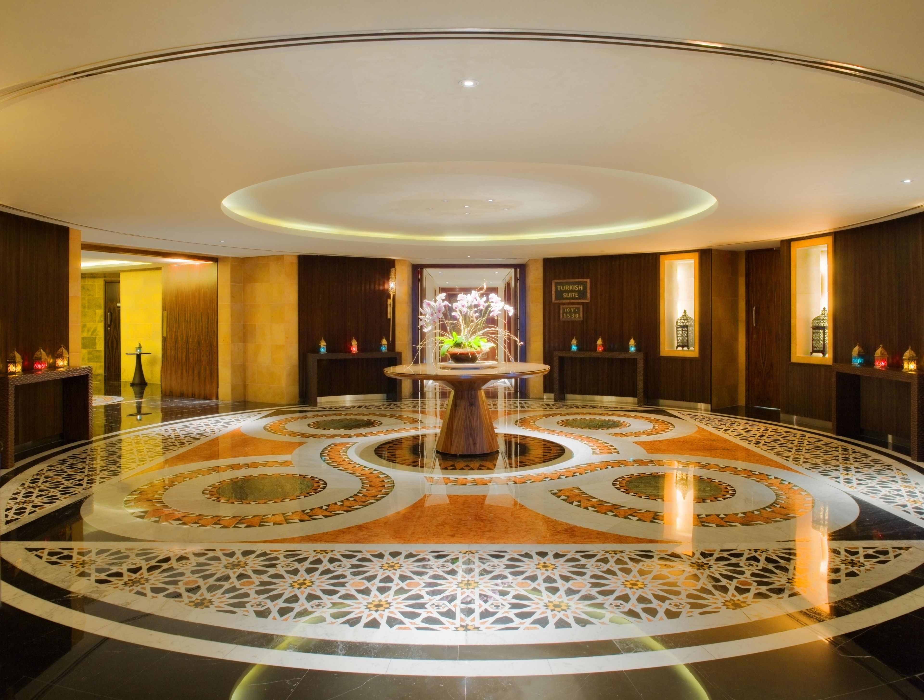 A hotel lobby with a central round table, a patterned floor, and wooden paneling.