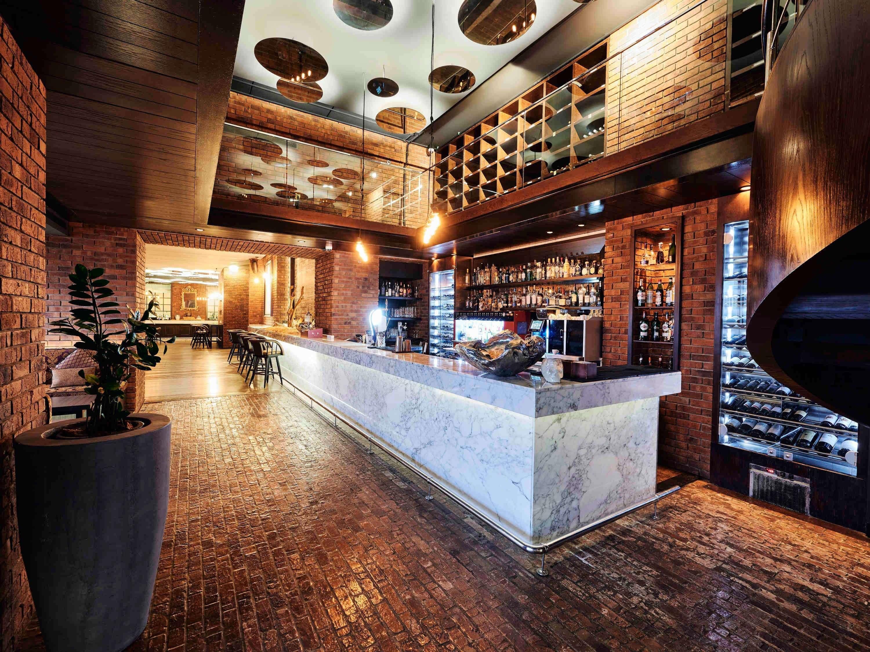 A bar area with a marble counter, brick walls, and a ceiling with circular light fixtures.