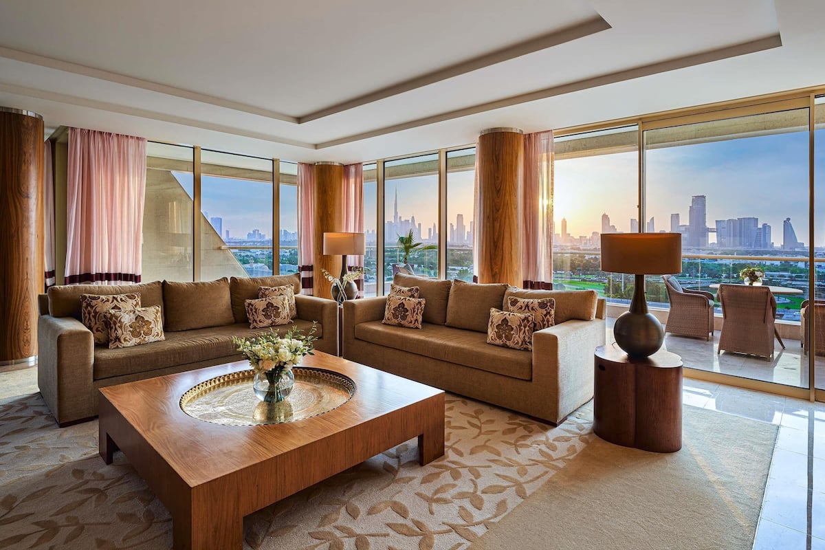 A spacious living room with a large window, a wooden coffee table, and two sofas with patterned cushions.