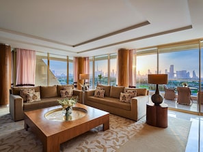 A spacious living room with a large window, a wooden coffee table, and two sofas with patterned cushions.