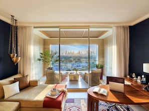 A modern living room with a large window, a sofa, a dining table, and a view of a city skyline. - Raffles Dubai (Dubai)