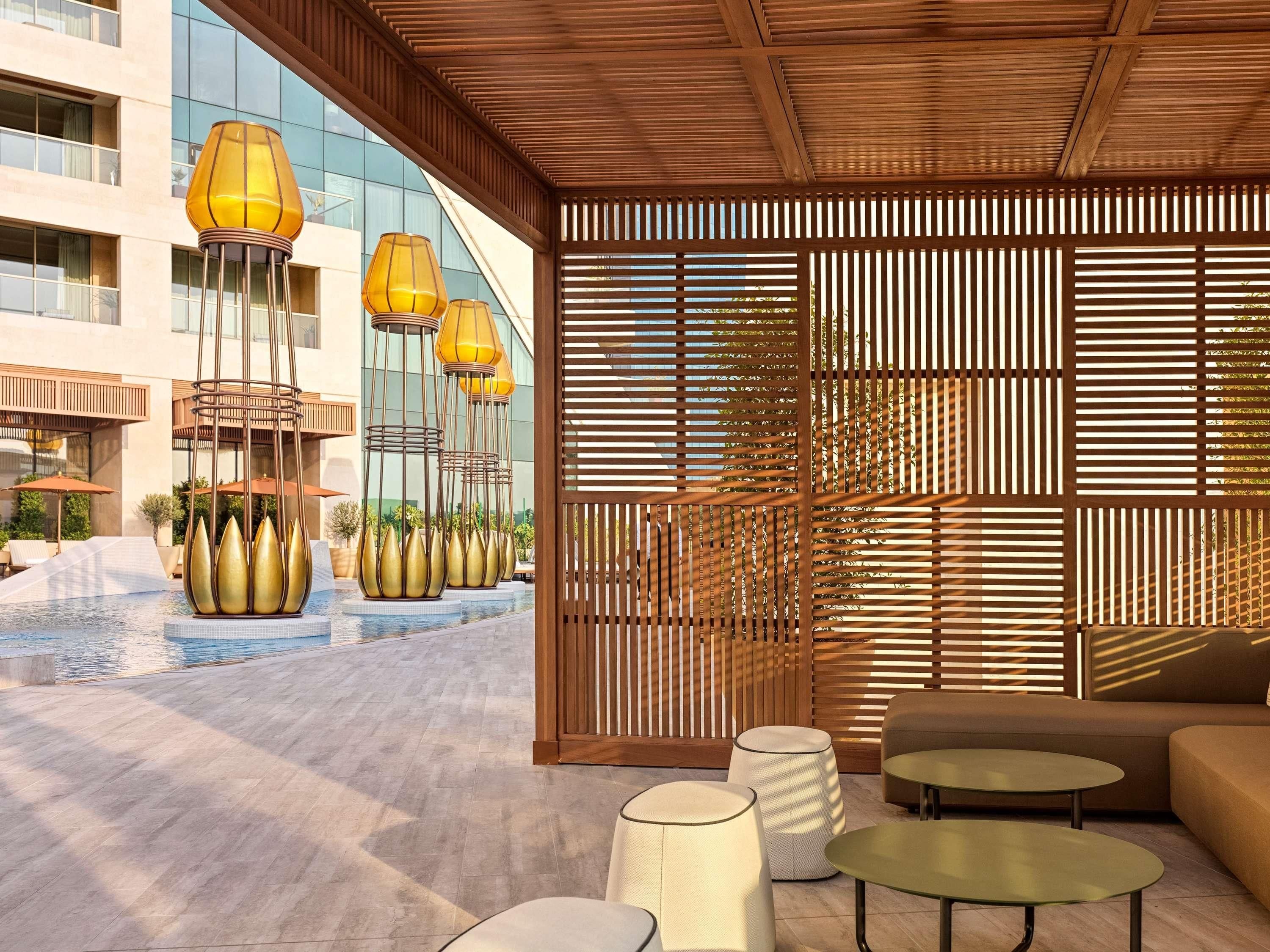 A modern outdoor seating area with a pool, wooden slats, and tall lamps.