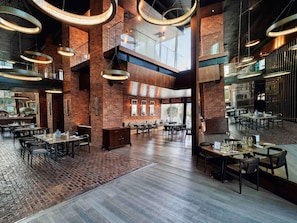 A spacious restaurant with high ceilings, exposed brick walls, and modern lighting fixtures. - Raffles Dubai (Dubai)