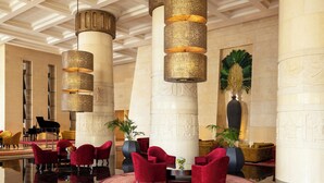 A lobby with red upholstered chairs, a grand piano, and a large decorative vase.
