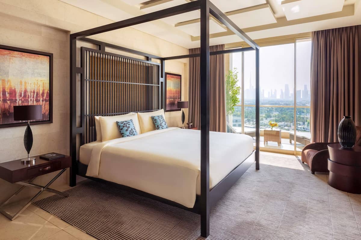 A modern hotel room with a four-poster bed, a city view, and a large painting on the wall.