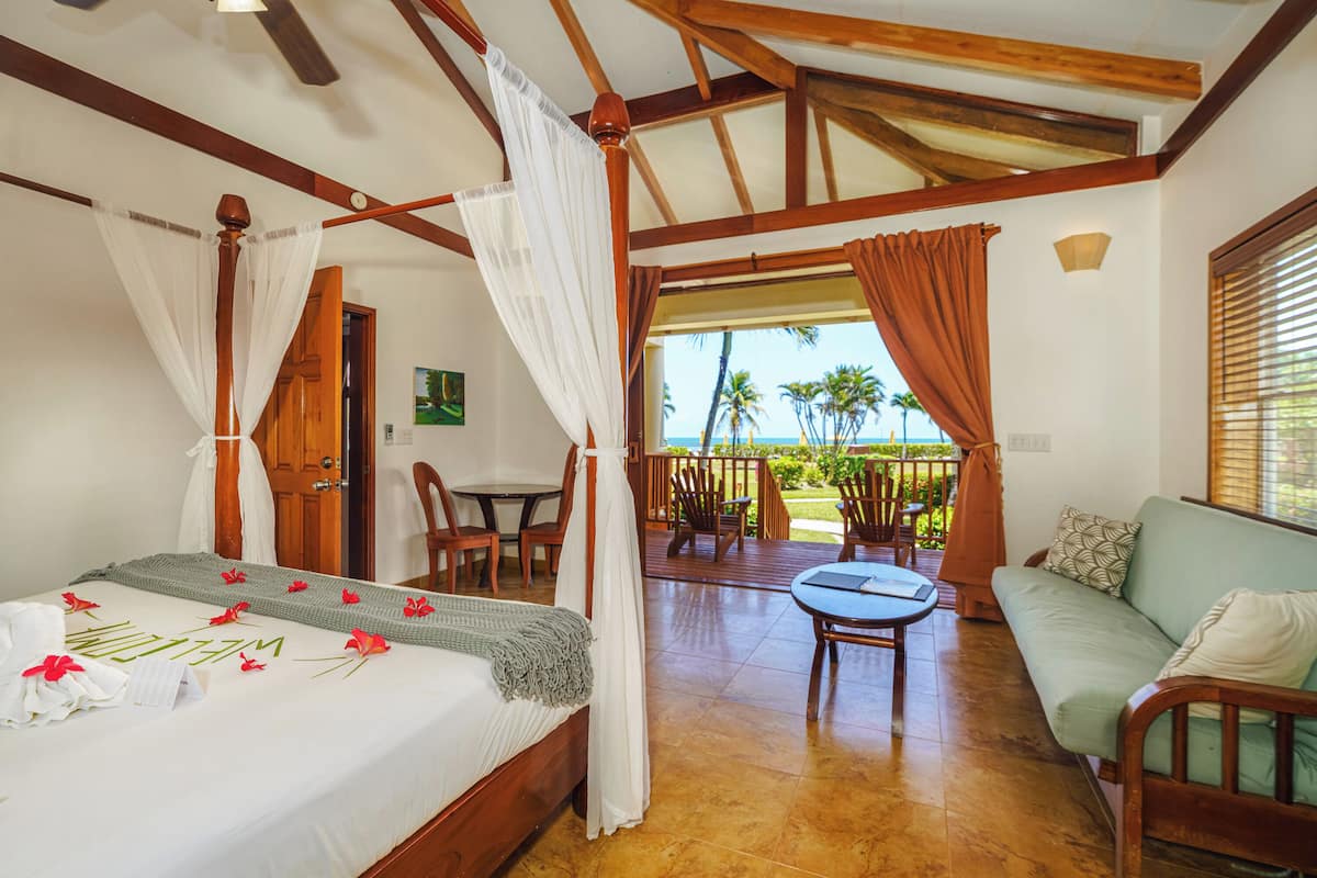 A room with a bed, a sofa, a table, and a balcony with chairs.