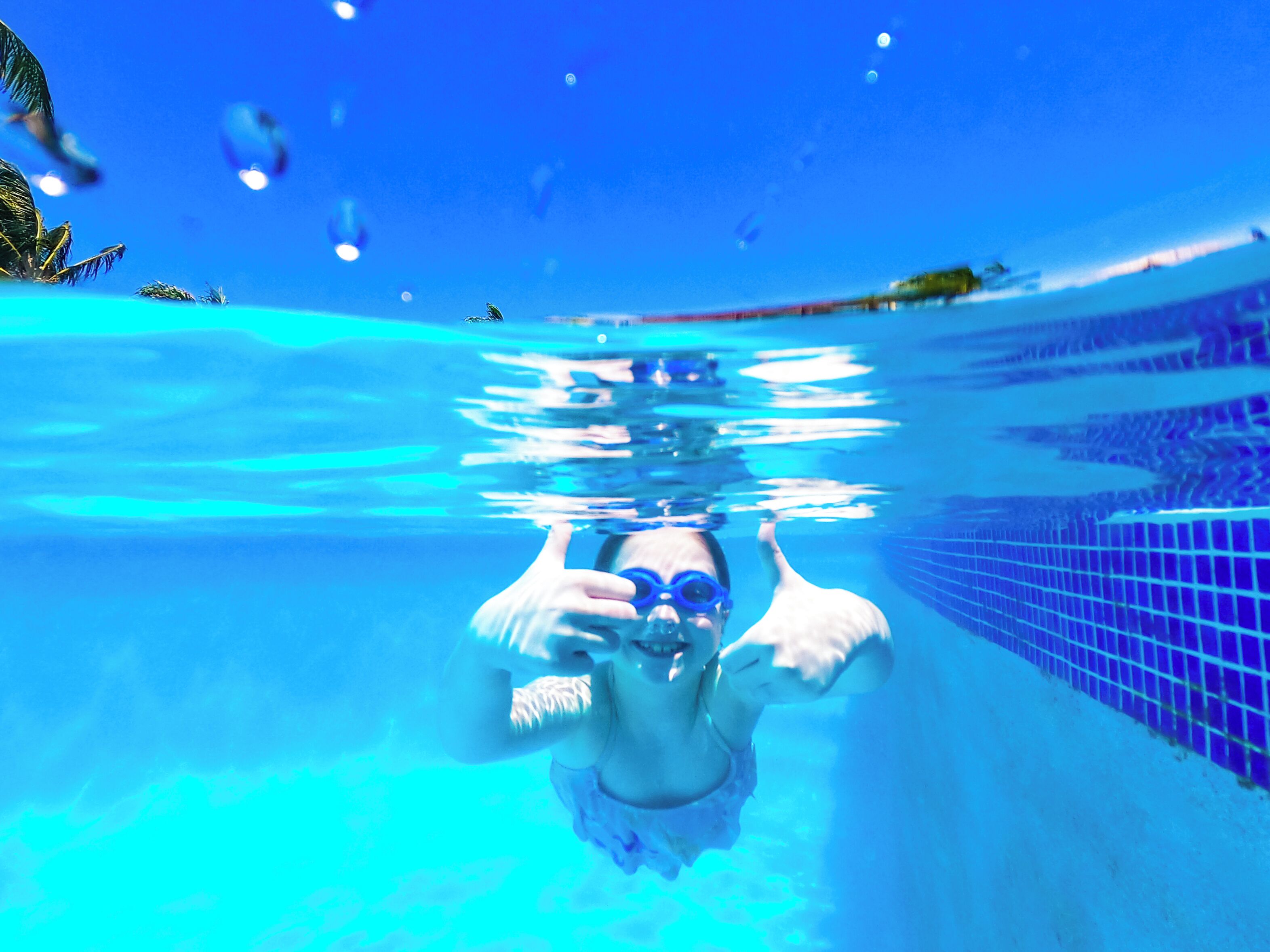 Une vue sous-marine d’une piscine, où l’on aperçoit une personne portant des lunettes de natation.