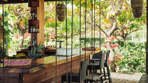 A wooden bar area with wicker chairs, a shelf with bottles, and a hanging basket. - Hopkins Bay Belize, a Muy'Ono Resort (Hopkins)