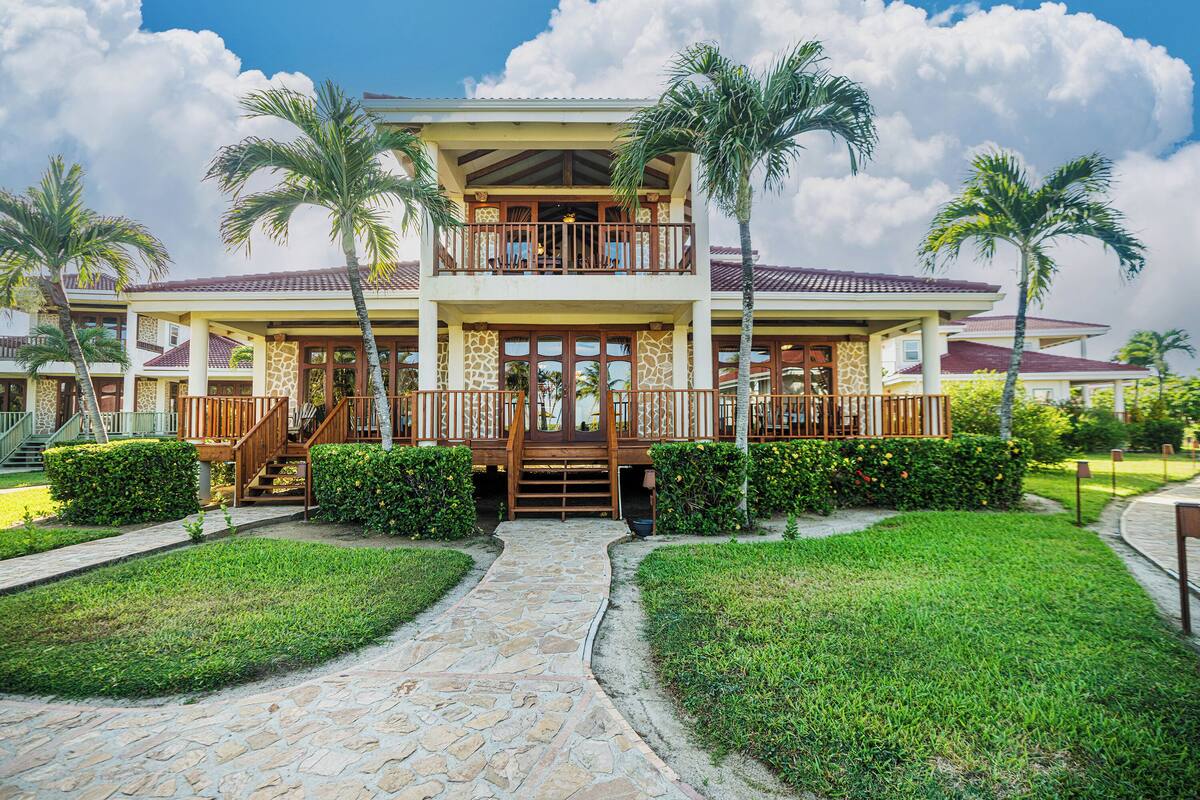 A two-story building with a central entrance, surrounded by palm trees and a stone pathway.