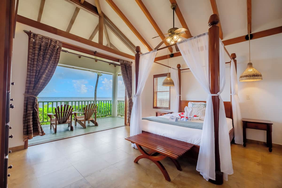 A bedroom with a bed, a bench, a bedside table, and a view of the sea.