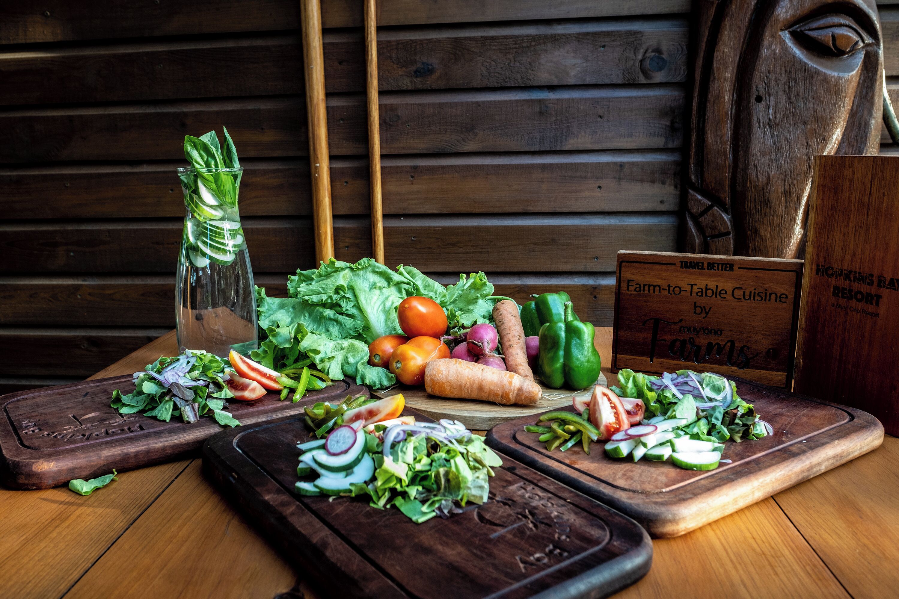 Un tavolo di legno con verdure fresche, una bottiglia di vetro e un cartello che illustra la cucina a chilometro zero.