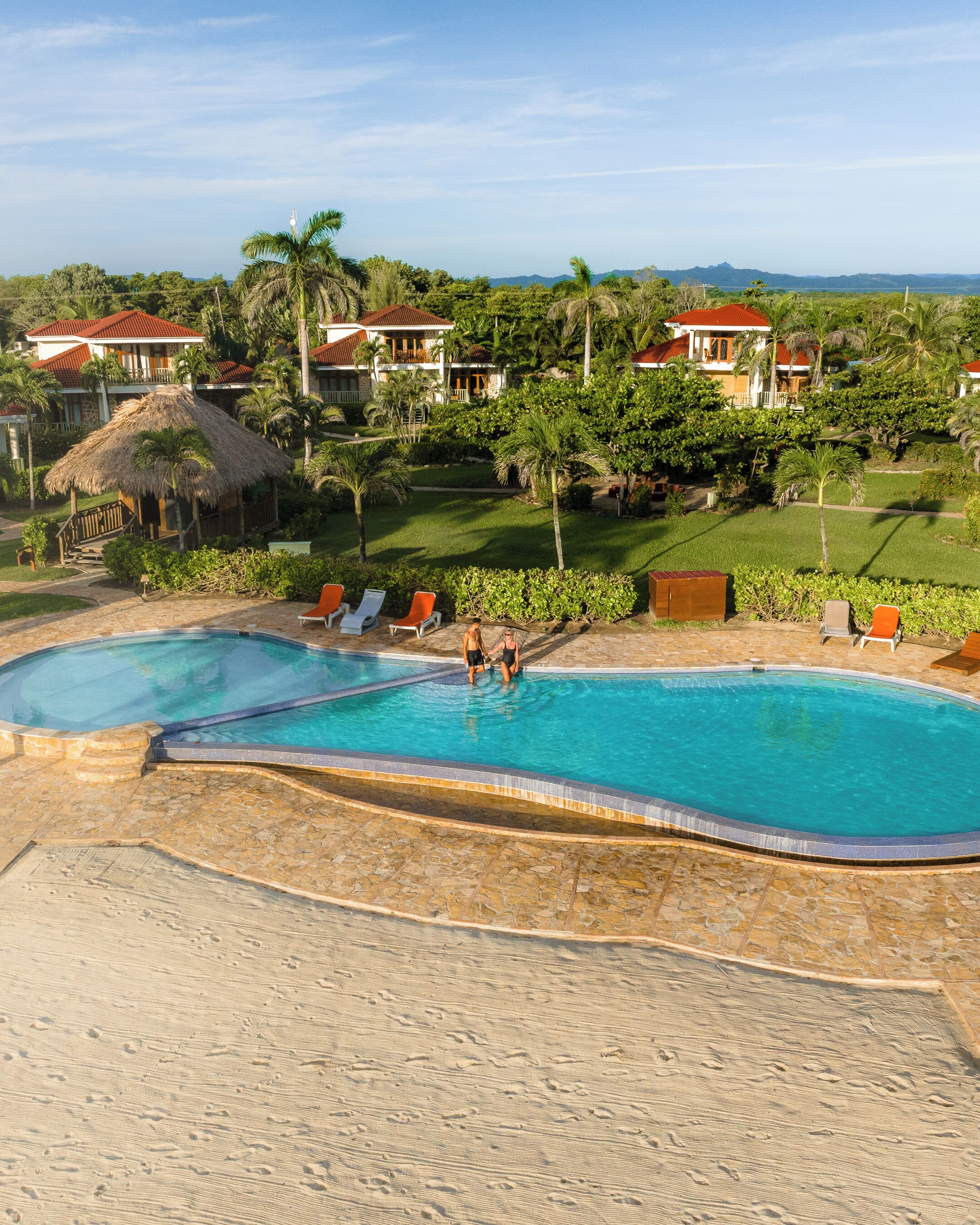 Un resort con piscina, lettini e una struttura con tetto di paglia.