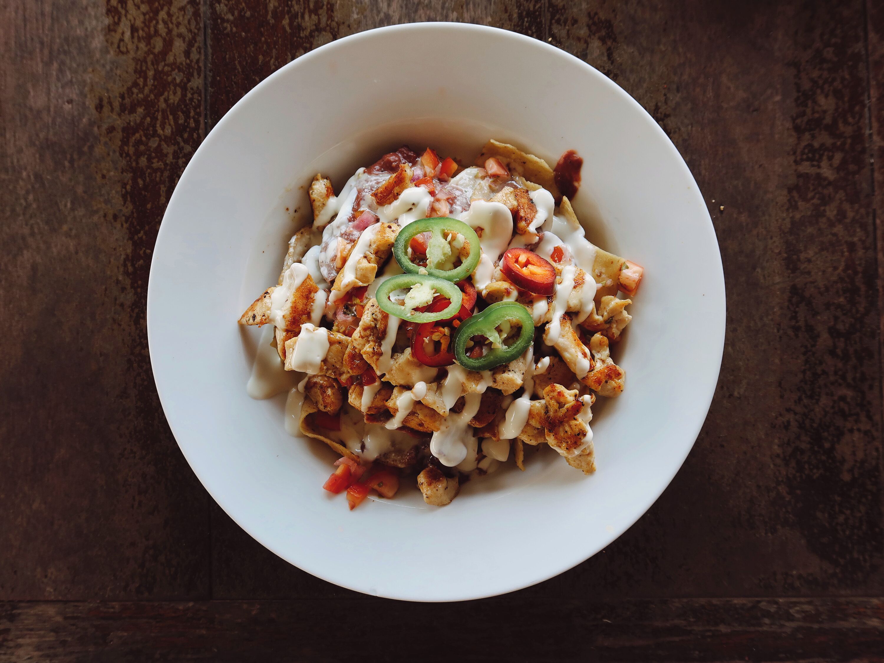 Een schaal nacho’s met kaas, jalapeño’s en een romige saus.
