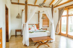 Una cama con dosel, un banco de madera, una mesita de noche y vistas al exterior a través de amplios ventanales.