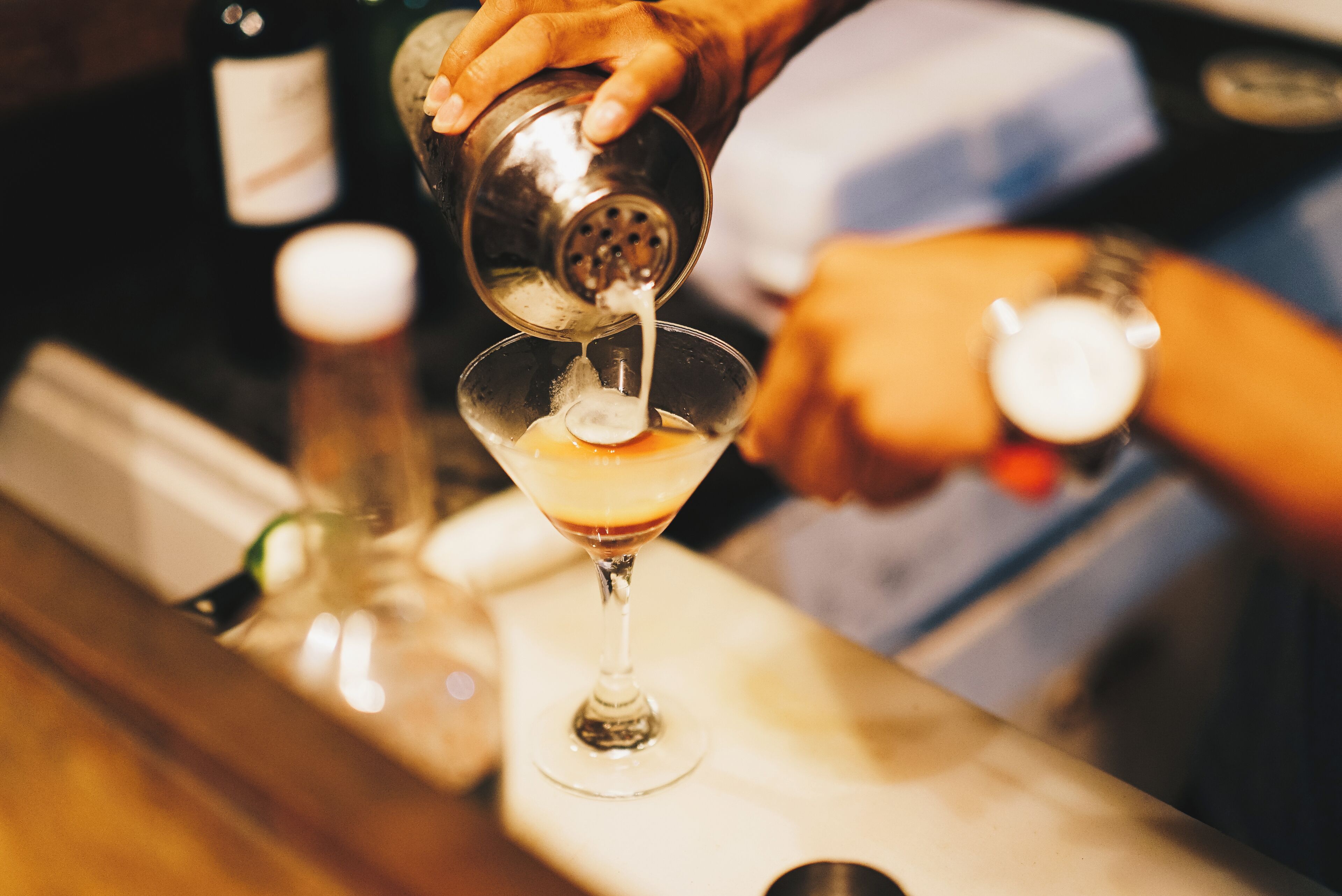 A bartender pouring a drink into a martini glass.