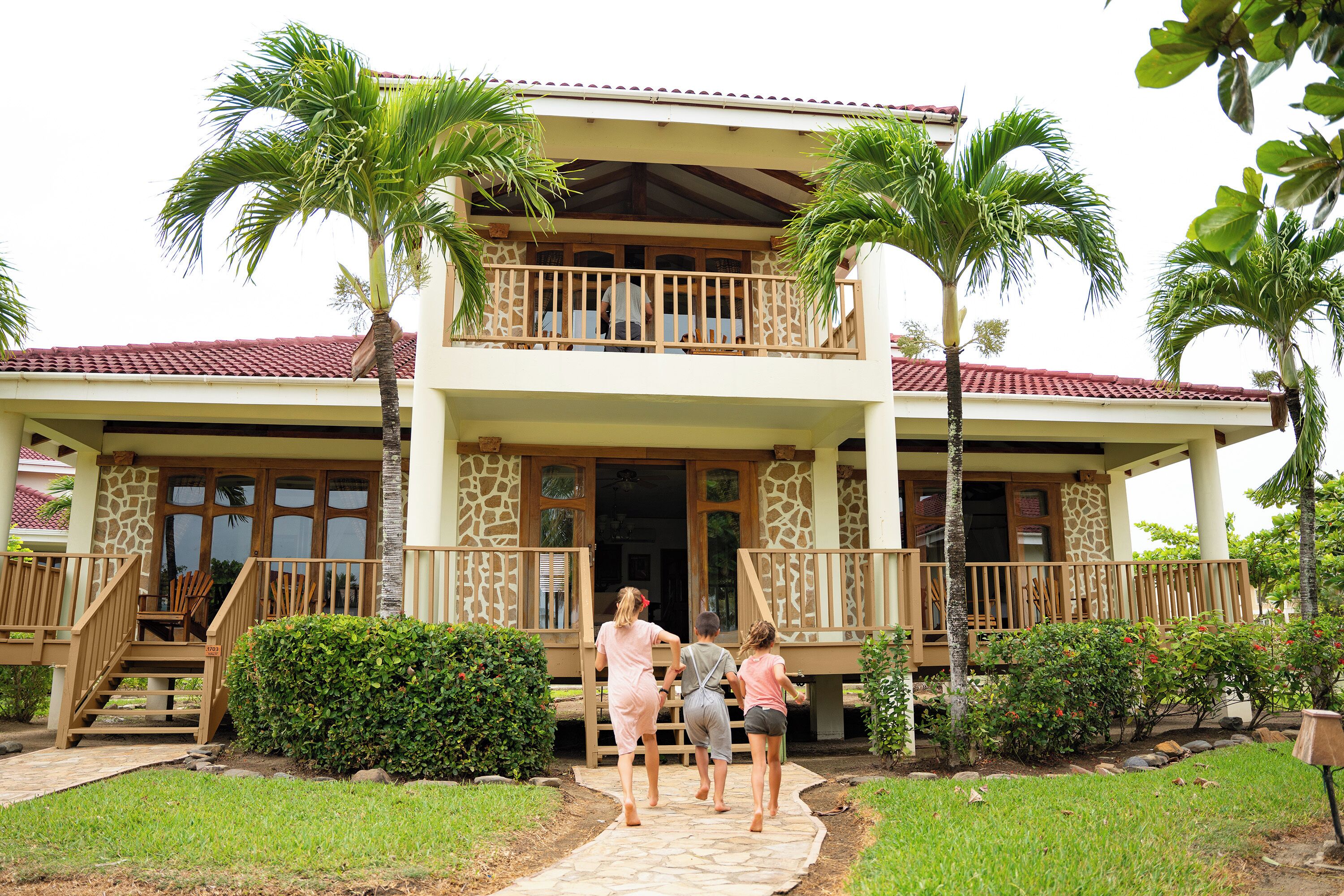 A two-story building with a balcony, palm trees, and a pathway leading to the entrance.